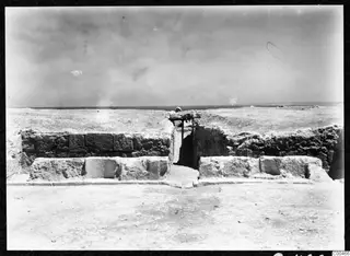 Ruined stone walls and seating blocks at the theatre at Soli, with bare ground in front and a band of sea on the horizon.