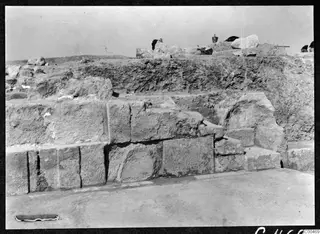 Excavated stone masonry at the theatre at Soli, with a bucket and loose stones on the bank behind.