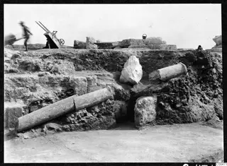 Column drums and a carved stone fragment lying among excavated earth and rubble at the theatre at Soli