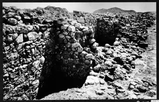Excavated stone walls and rubble at Soli, with a dark recess between the walls and hills in the background.