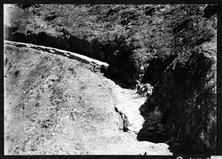Excavation cutting at the Soli theatre, with a curved stone wall along the upper left edge and loose stones in the channel below