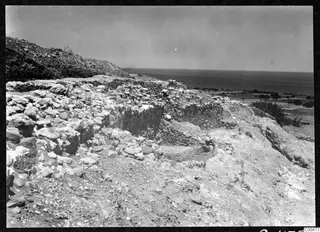 Excavated stone walls at Soli with a scrubby hillside on the left and the sea beyond the coastal plain