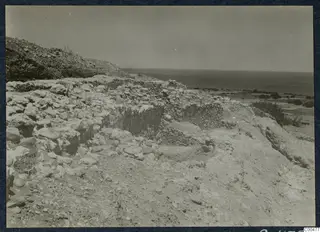 Ruined stone walls on a stony slope at Soli, with a hillside behind and the sea beyond.