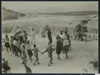 People dancing in a circle on the orchestra of the theatre at Soli, with seated musicians at right
