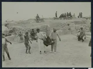 People in the excavated theatre at Soli, with a seated man playing an instrument and wheelbarrows on the sand