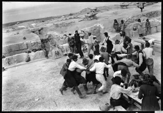 Men linked arm in arm in a line across excavated ground at Soli, with wheelbarrows and stone blocks behind them