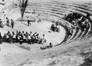 Festival in the orchestra of the theatre at Soli, with men seated on a long bench and spectators on the tiers.