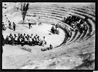 Festival in the orchestra of the theatre at Soli, with people seated on a bench and on the stone tiers