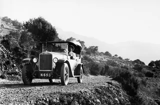 Open-top Volvo car with three passengers driving on a gravel road through hillside scrub in the Kyrenia Mountains