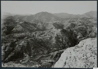 Wide view over hills and mountain ridges with terraced slopes, seen from a pale rocky outcrop in the foreground.
