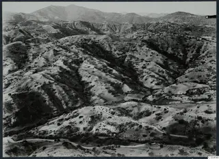 Aerial view of hilly, scrubby terrain with winding roads, with mountains beyond, near Vouni Palace.