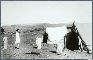 Two tents at Vouni with three stone sculptures set outside and a woman in a light dress standing at left