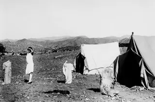 Two tents at Vouni with a woman in a light dress and three damaged stone sculptures set up outside