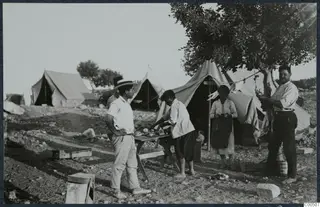 Camp tents and five people beside a table with food and plates at Vouni, under a tree