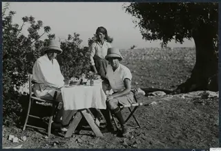 Breakfast laid on a white-clothed table at Vouni, with two men in sun helmets seated and a woman standing behind them.
