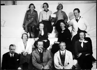 Group photograph of eleven people posed on white steps against a pale backdrop, including a girl, women and men.