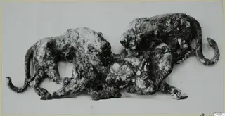Corroded bronze sculpture of two animals in one group, one rising above the other, with curled tails