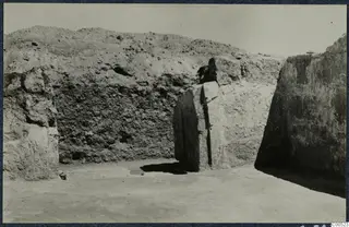 Large stone blocks and an upright stone slab in an excavation trench at Vouni, with an earth bank behind