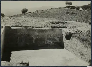 Excavation at Vouni palace, with a cleared stone wall face, a trench floor and shrubs on the hillside