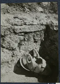 Broken two-handled vessel lying in excavated ground at Vouni Palace, with a layered earth face behind it