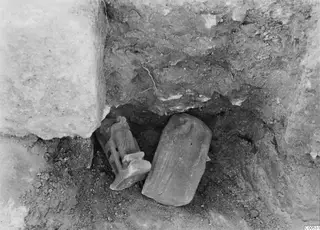 Finds in situ at Vouni Palace: a small figure and a rounded object lying in soil beside a large stone block.