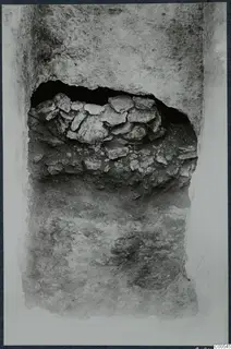 Excavated cutting with a heap of flat stones set into an opening in a soil face, at Vouni
