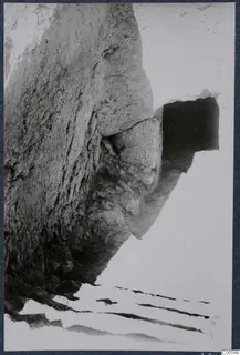 Excavated rock face with a dark rectangular opening and flat stone slabs at Vouni