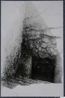 Excavation cutting at Vouni with a rubble stone wall and a dark stepped opening in the earth