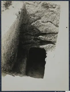 Cutting leading down to a dark rectangular doorway in layered rock at Vouni