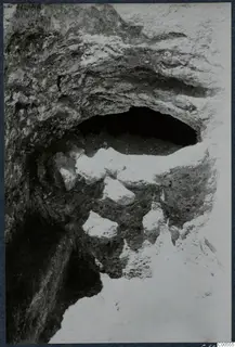 Excavated arched opening in a rough cut face at Vouni, with pale stones lying on a soil ledge