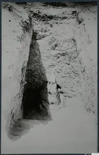 Narrow excavation trench at Vouni with a dark opening and steps at the left and a pale stone at the centre.