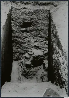 Narrow excavation trench at Vouni with a tall rough wall face and stones at its base