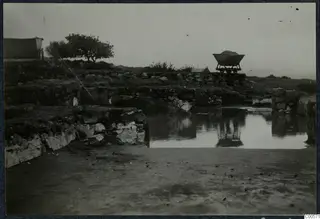 Rain water standing among stone walls of the palace at Vouni, with a rail wagon on a track behind.