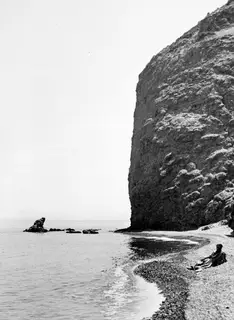 Steep rocky cliff above a pebble beach at Vouni, with the sea and a small offshore rock to the left.