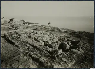 Rails, stone blocks and a small tree at the palace at Vouni, with the sea beyond
