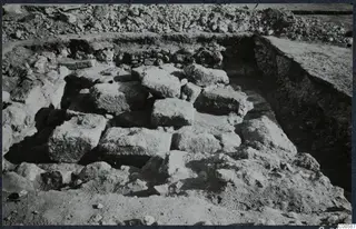 Excavated stone blocks and rubble at Vouni palace, with a trench and spoil heap behind.