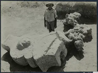 Boy in a wide-brimmed hat standing beside large worked stone blocks lying in situ at Vouni