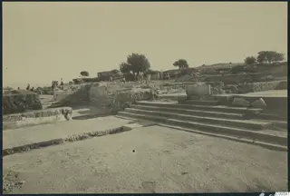 Stone steps and low walls at Vouni Palace, with people standing among the ruins and trees behind