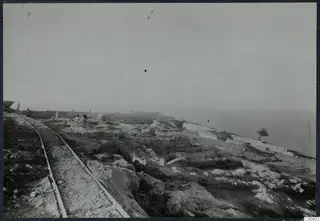 Excavation at the Vouni palace with a rail track running past trenches and cut stone walls toward the sea.