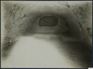 Interior of a rock-cut chamber with a vaulted ceiling, a rectangular slab in the far wall and a low ledge along the back.