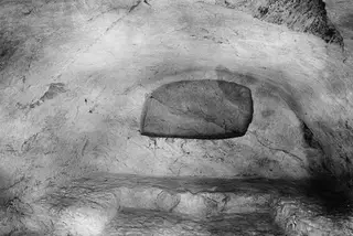 Interior of rock-cut Tomb 8 at Vouni, with a rectangular stone slab set into the back wall.
