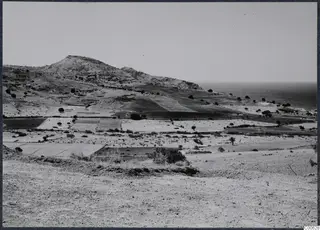 View across fields and scrub from the acropolis of Soli towards a rocky hill and the sea.