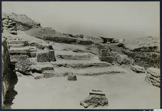 Stone steps cut into an excavated slope at Vouni Palace, with squared blocks and a wheelbarrow on the spoil heap above