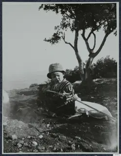 Stefan Gjerstad sitting outside the house at Vouni in striped clothes and a sun hat, holding a long stick.