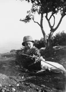 Stefan Gjerstad, a young boy in a striped top and bucket hat, sitting on stony ground beside a tree at Vouni.