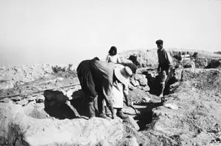 Four people working at the excavation at Vouni, with rails and stone walls in the trench.