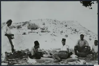 Five people outdoors at Vouni, with two men resting on a striped mattress and drinking tea.