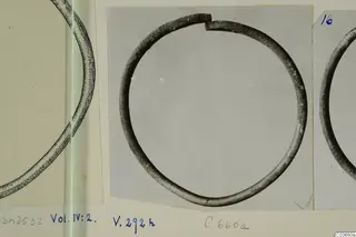 Silver bracelet, an open ring with a gap at the top, photographed on a grey card mount beside other drawings and photographs.