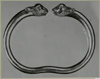 Gold bracelet with an animal head at each open end, photographed against a grey backdrop