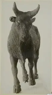 Bronze statuette of a horned animal, perhaps a bull, standing on a wooden board.